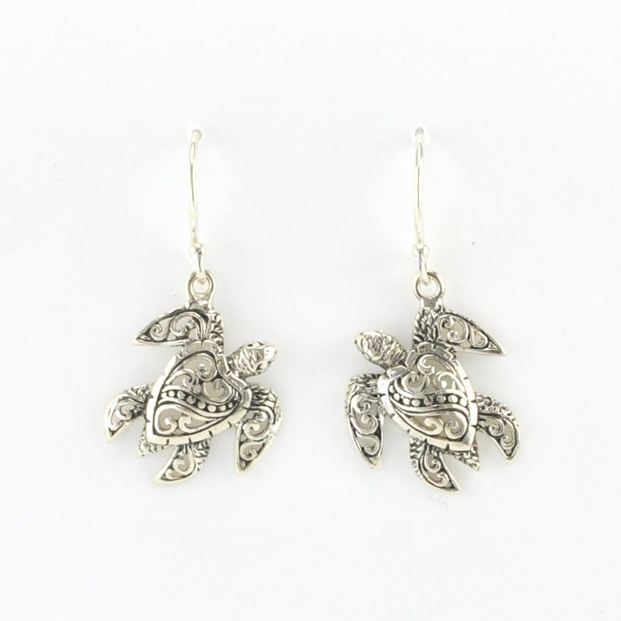 A pair of silver-toned sea turtle drop earrings with intricate filigree detailing, shown against a plain white background.