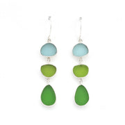 A pair of silver drop earrings featuring three stacked, organic-shaped sea glass stones in light blue, olive green, and medium green, shown against a plain white background.