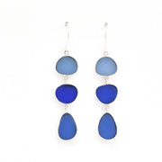 A pair of drop earrings featuring three stacked, organic-shaped glass pieces in shades of blue (light blue, royal blue, and deep cobalt blue) set in silver-tone metal with fishhook backings, shown against a plain white background.