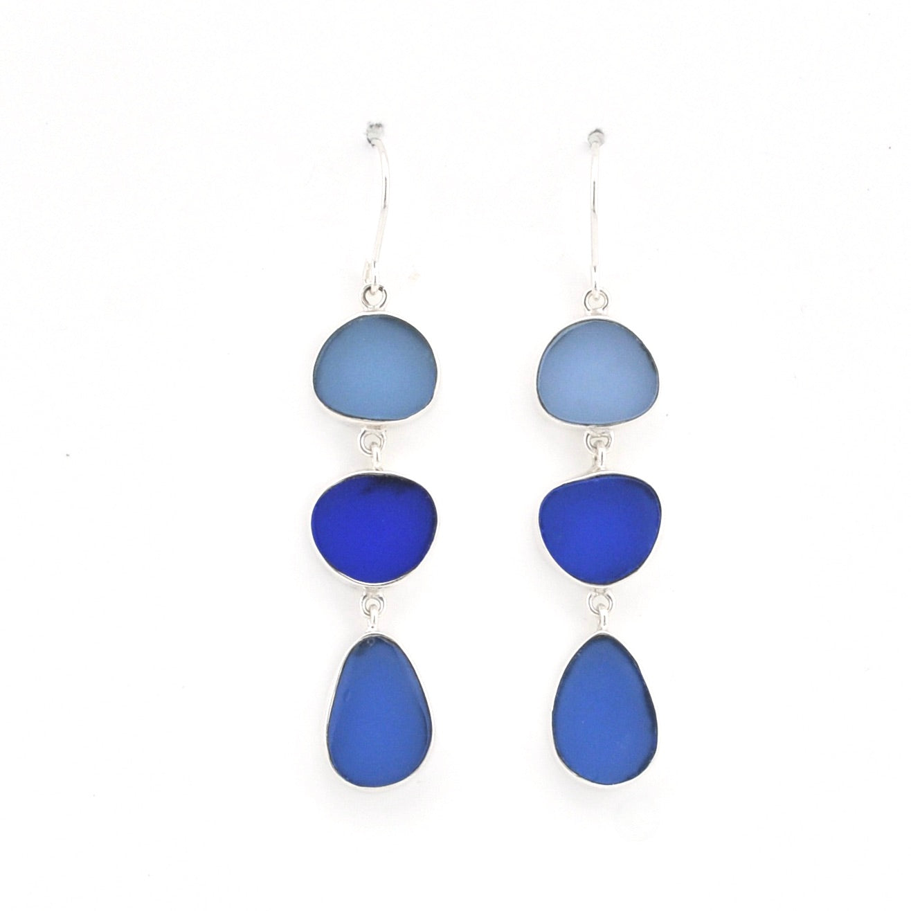 A pair of drop earrings featuring three stacked, organic-shaped glass pieces in shades of blue (light blue, royal blue, and deep cobalt blue) set in silver-tone metal with fishhook backings, shown against a plain white background.