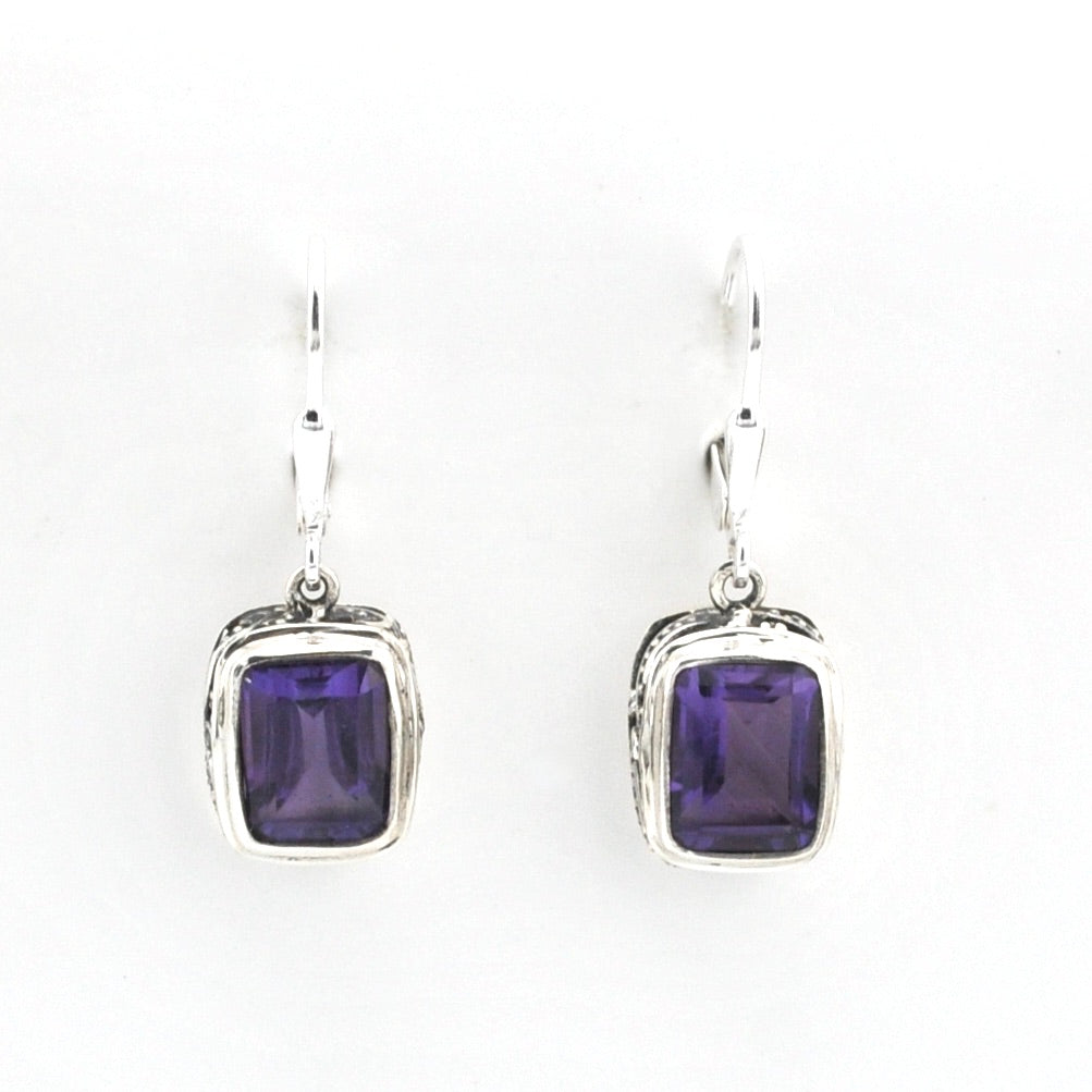 Pair of silver earrings with purple gemstones on a white background
