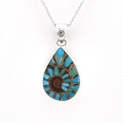 A teardrop-shaped pendant necklace featuring a natural ammonite gemstone with a spiral pattern of turquoise blue and brown set in a silver bezel on a silver chain against a white background.