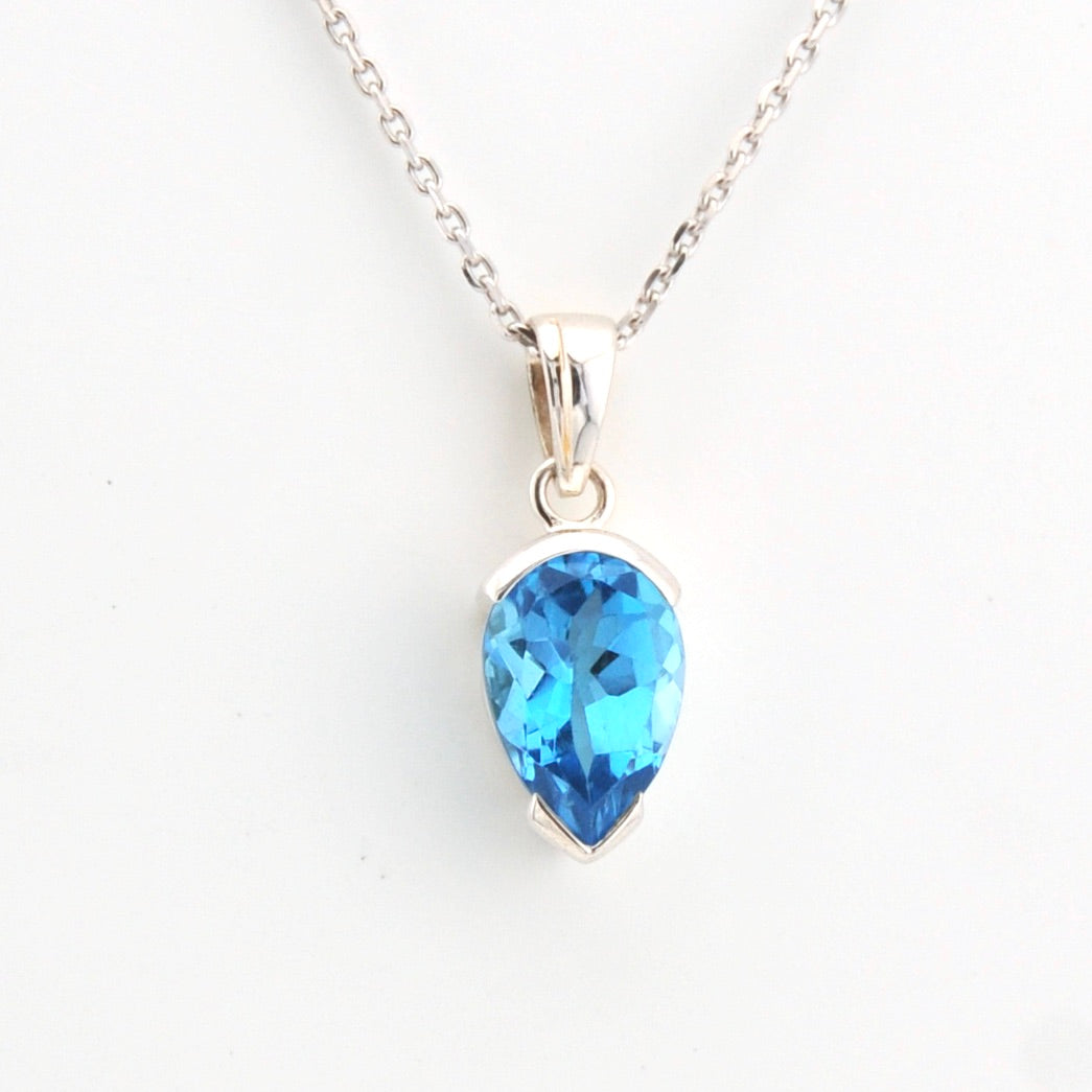 Teardrop-shaped blue gemstone pendant on a silver chain against a white background