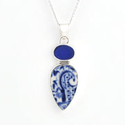 A silver pendant necklace featuring a teardrop-shaped blue and white patterned porcelain pendant and a smaller oval blue stone above it, on a white background.