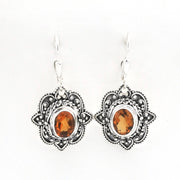 A pair of silver-toned bohemian dangle earrings with ornate filigree details and oval amber-orange gemstones, shown on a plain white background.