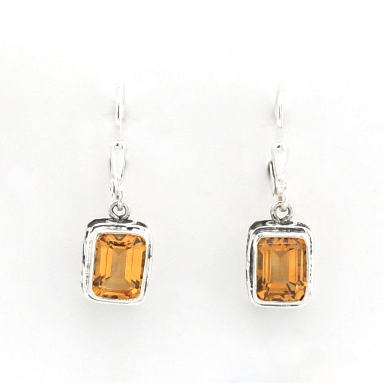 A pair of silver drop earrings featuring rectangular emerald-cut amber gemstones in a textured bezel setting, suspended from silver French hooks against a plain white background.