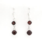 A pair of silver drop earrings with two dark red gemstones in a square bezel setting, hanging from silver fishhook wires on a plain white background.