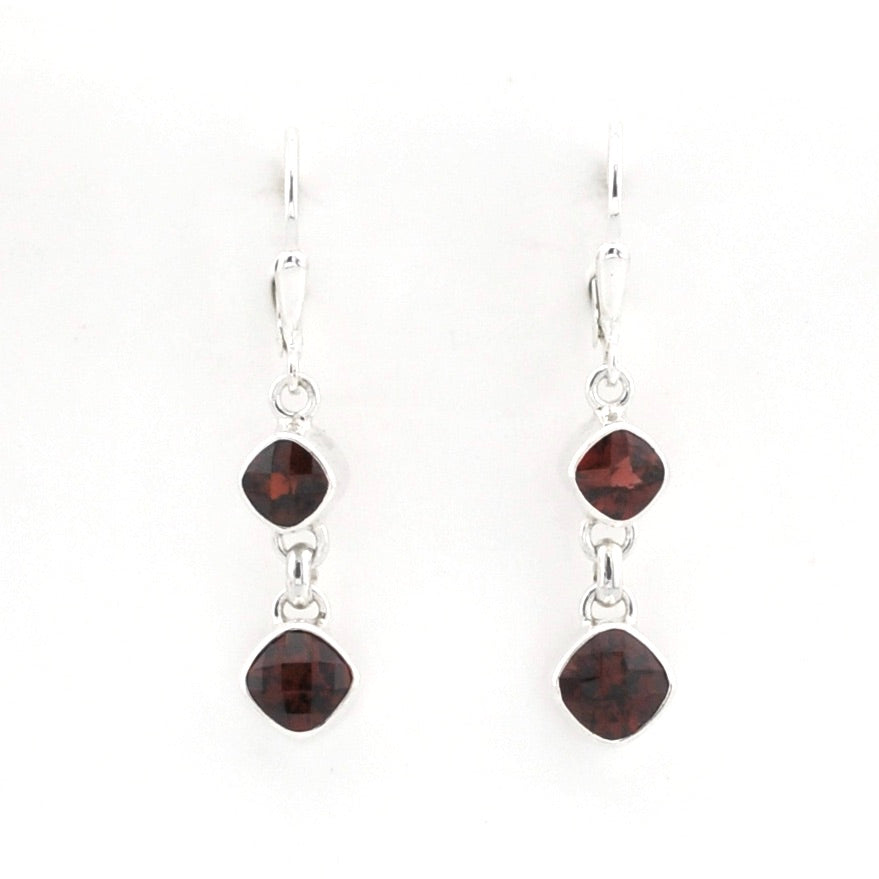 A pair of silver drop earrings with two dark red gemstones in a square bezel setting, hanging from silver fishhook wires on a plain white background.
