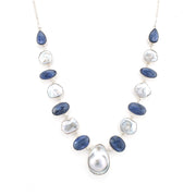 A silver-tone necklace featuring alternating polished dark blue oval stones and irregular white keshi pearls, with a large teardrop pearl pendant at the center, shown on a plain white background.