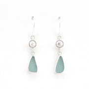 A pair of silver drop earrings featuring a small white pearl bead and a teardrop-shaped sea glass drop in a light blue-green color, set against a plain white background.