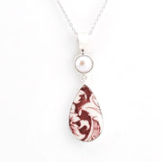 A silver pendant necklace featuring a round white pearl and a teardrop-shaped pendant with a marbled burgundy and white pattern, shown on a plain white background.