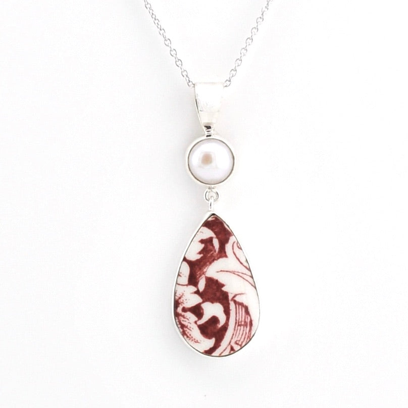 A silver pendant necklace featuring a round white pearl and a teardrop-shaped pendant with a marbled burgundy and white pattern, shown on a plain white background.