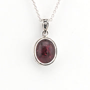 Silver pendant with a red gemstone on a white background