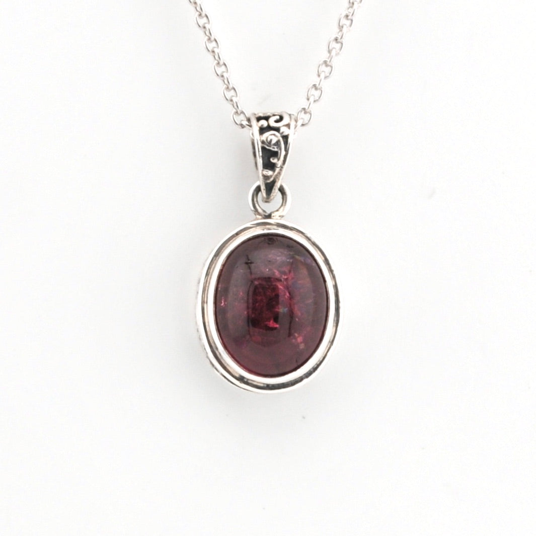 Silver pendant with a red gemstone on a white background