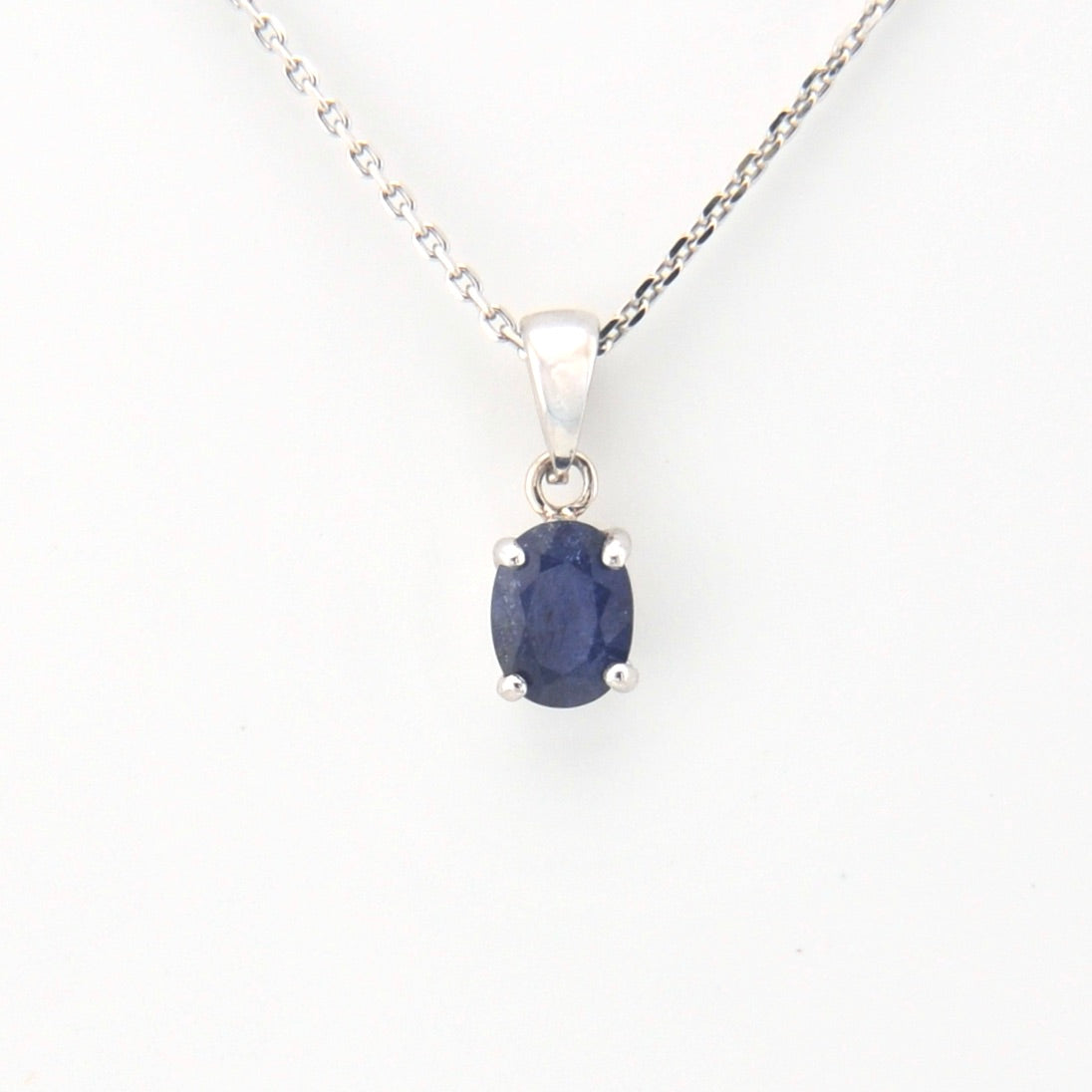Sapphire pendant on a silver chain against a white background