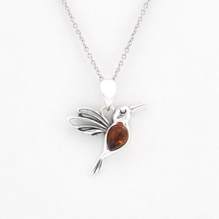 A sterling silver hummingbird pendant necklace with a polished amber gemstone in its body, suspended from a delicate silver chain against a plain white background.