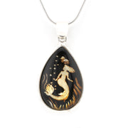 A teardrop-shaped pendant necklace featuring a mermaid design in gold over a black background, suspended from a silver-toned chain on a white background.