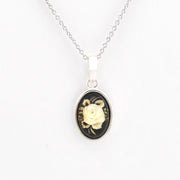A silver chain necklace with an oval pendant featuring a cream-colored rose carved over a black background, set in a silver bezel.