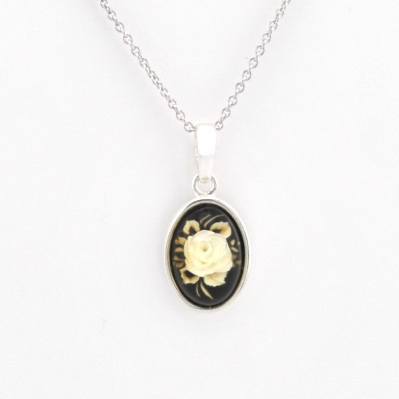 A silver chain necklace with an oval pendant featuring a cream-colored rose carved over a black background, set in a silver bezel.