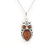 A silver owl pendant necklace featuring a large amber teardrop-shaped center stone and two smaller round amber stones for eyes, suspended from a silver chain against a plain white background.