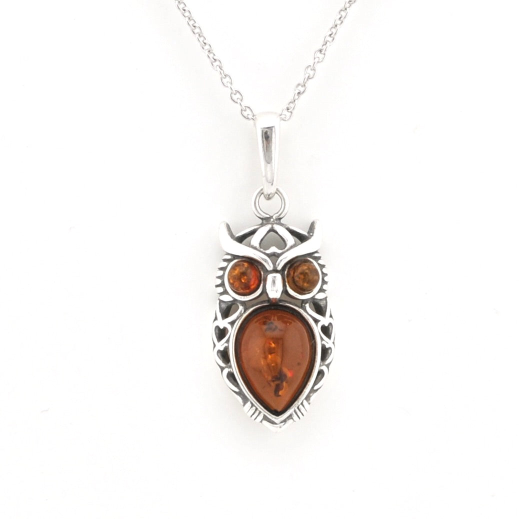 A silver owl pendant necklace featuring a large amber teardrop-shaped center stone and two smaller round amber stones for eyes, suspended from a silver chain against a plain white background.