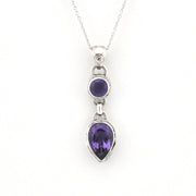 A silver pendant necklace featuring a teardrop-shaped purple gemstone and a smaller oval purple gemstone set in a silver bezel, suspended from a delicate silver chain against a white background.