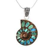 A spiral ammonite fossil pendant necklace with inlaid blue and green opal stones in a silver-toned setting, suspended from a silver chain against a white background.