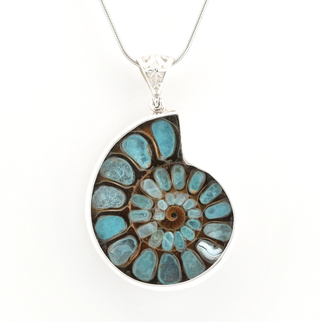 A silver pendant necklace featuring a spiral ammonite fossil inlay with turquoise blue, brown, and white natural stone patterns, suspended on a silver chain against a white background.