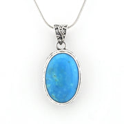 An oval pendant necklace featuring a vibrant blue cabochon gemstone in a silver bezel setting, suspended from a silver snake chain against a plain white background.
