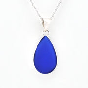 A teardrop-shaped cobalt blue glass pendant necklace on a silver chain, shown against a plain white background.