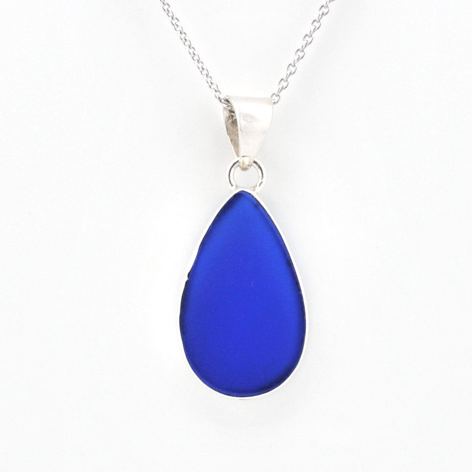 A teardrop-shaped cobalt blue glass pendant necklace on a silver chain, shown against a plain white background.