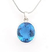 A round-cut blue gemstone pendant in a silver bezel setting on a silver snake chain, shown against a plain white background.