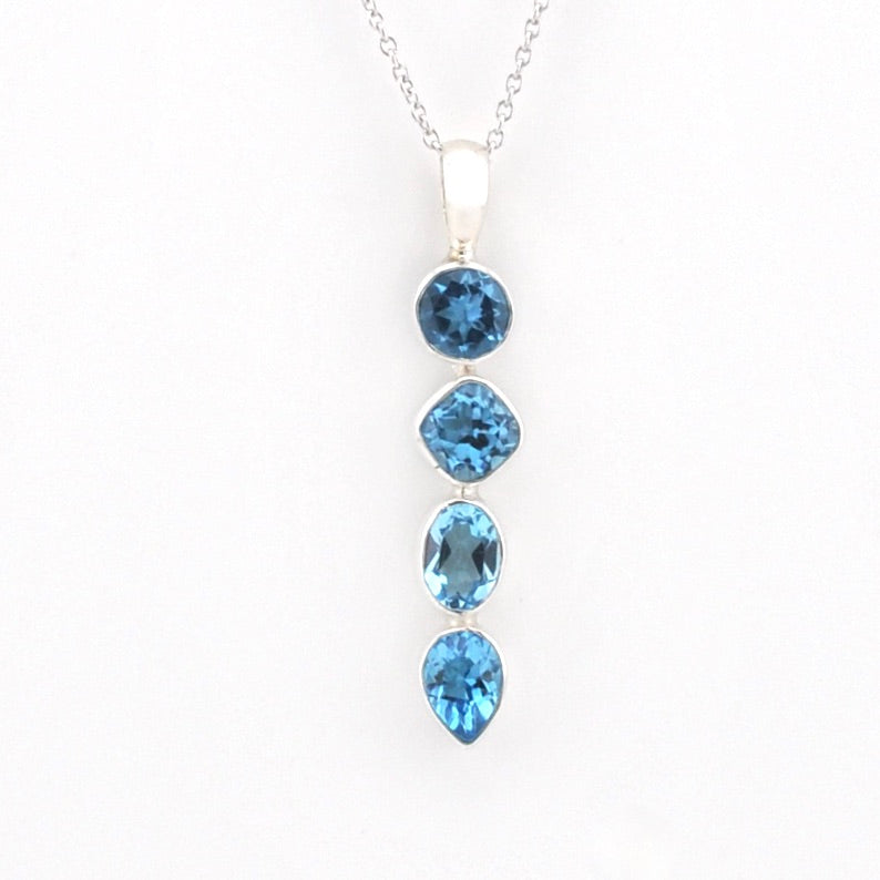 A silver pendant necklace featuring four cascading blue gemstones in round, cushion, oval, and teardrop shapes on a plain white background.