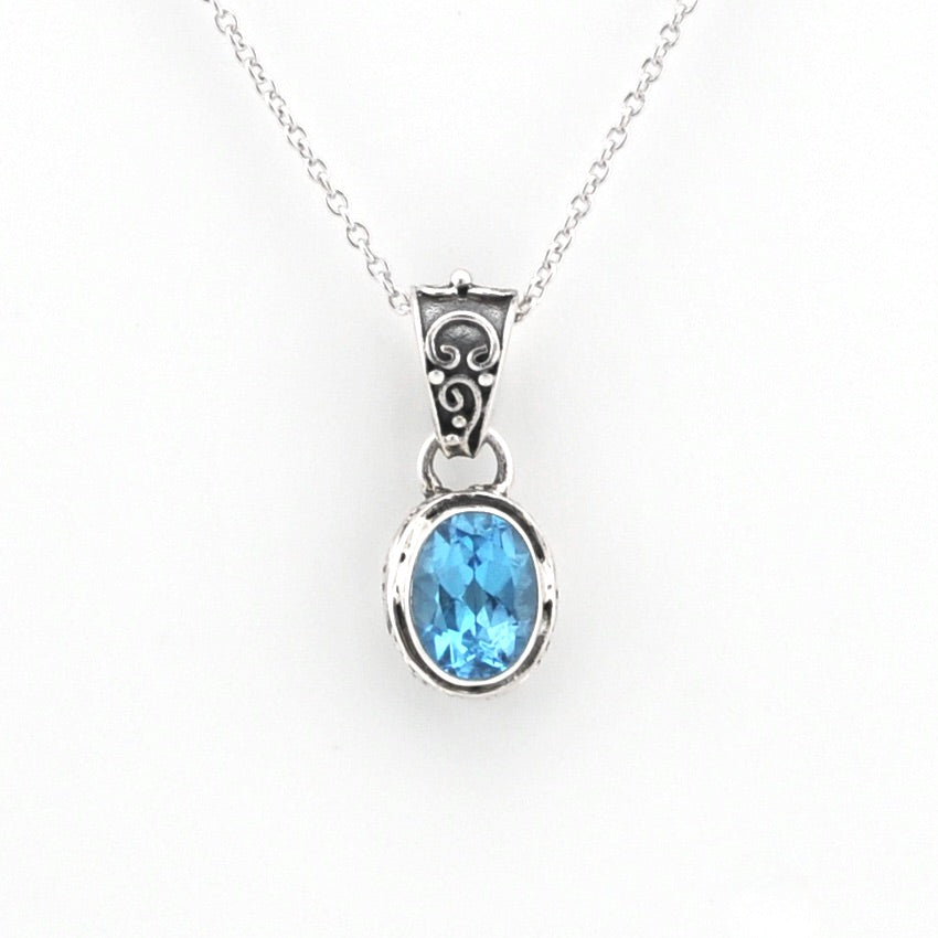 A silver pendant necklace featuring an oval-cut light blue gemstone in a silver bezel setting, suspended from a delicate silver chain against a plain white background.