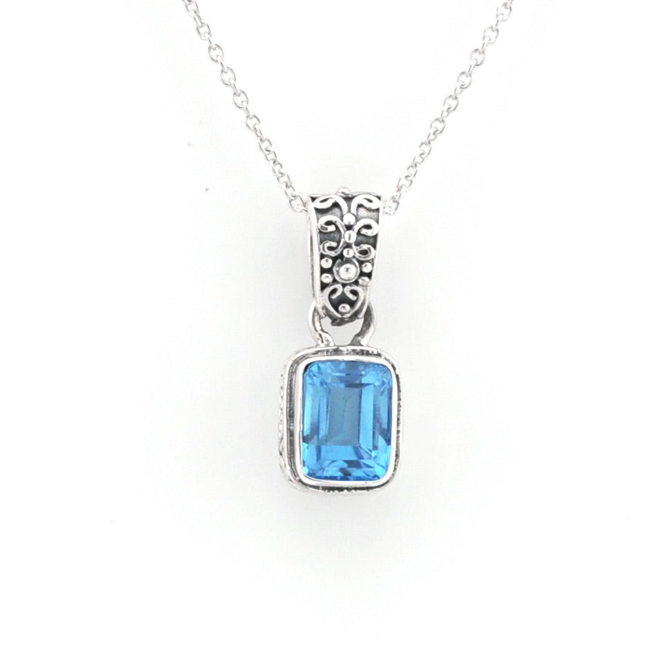 A silver pendant necklace featuring a rectangular light blue gemstone in a silver bezel setting with an ornate filigree bail, suspended from a delicate silver chain against a plain white background.