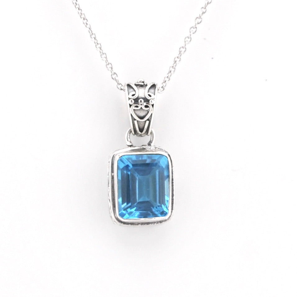 A silver pendant necklace featuring a rectangular emerald-cut blue gemstone in a silver bezel setting, suspended from a delicate silver chain against a plain white background.