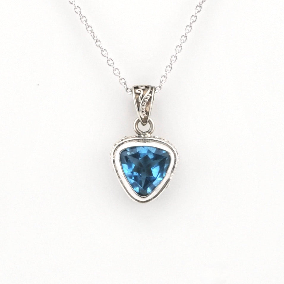 A silver pendant necklace featuring a faceted triangular blue gemstone in a silver bezel setting, suspended from a delicate silver chain against a plain white background.