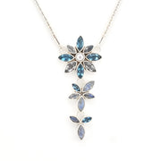 A silver-tone floral dangle necklace featuring three cascading flower pendants with marquise-cut blue gemstones and a central round clear stone on a white background.