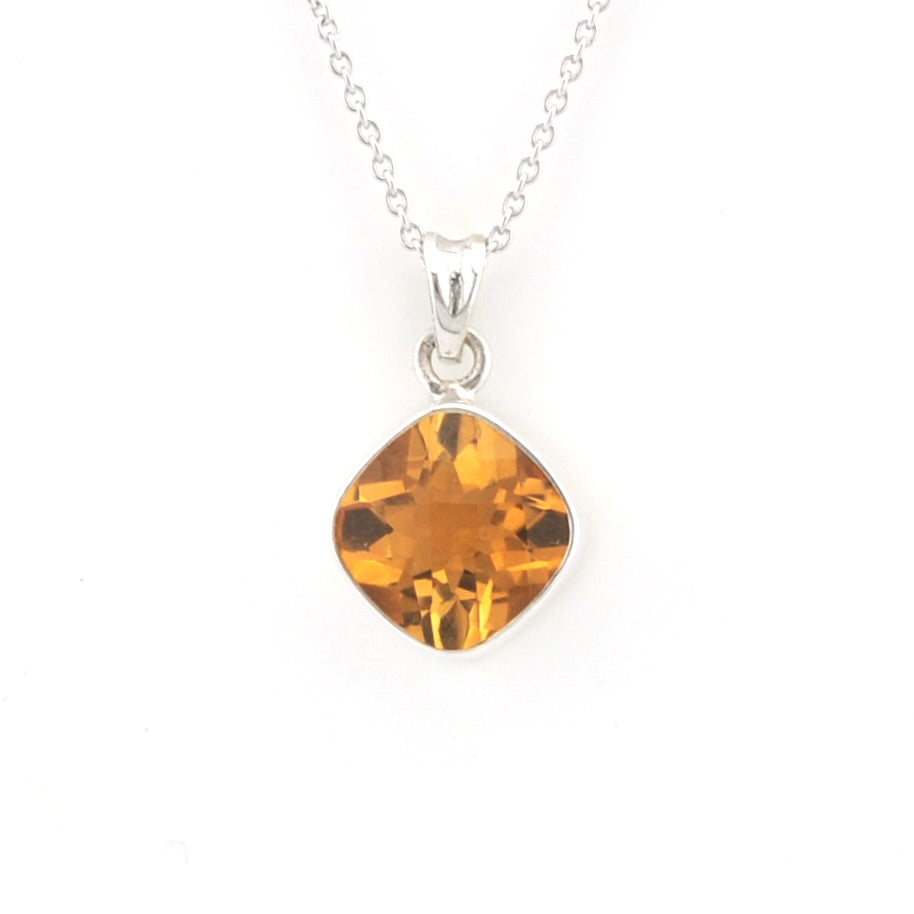 A silver necklace with a cushion-cut orange gemstone pendant, displayed against a solid white background.