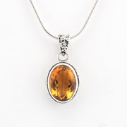 A silver pendant necklace featuring an oval-cut orange-yellow gemstone in a silver bezel setting, suspended from a silver snake chain against a plain white background.