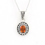 A silver pendant necklace featuring a oval-cut orange gemstone surrounded by a textured, oxidized silver border and a decorative filigree bail, suspended from a silver chain on a white background.