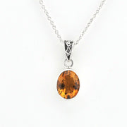 An oval citrine gemstone pendant necklace in a silver bezel setting on a delicate silver chain, shown against a plain white background.