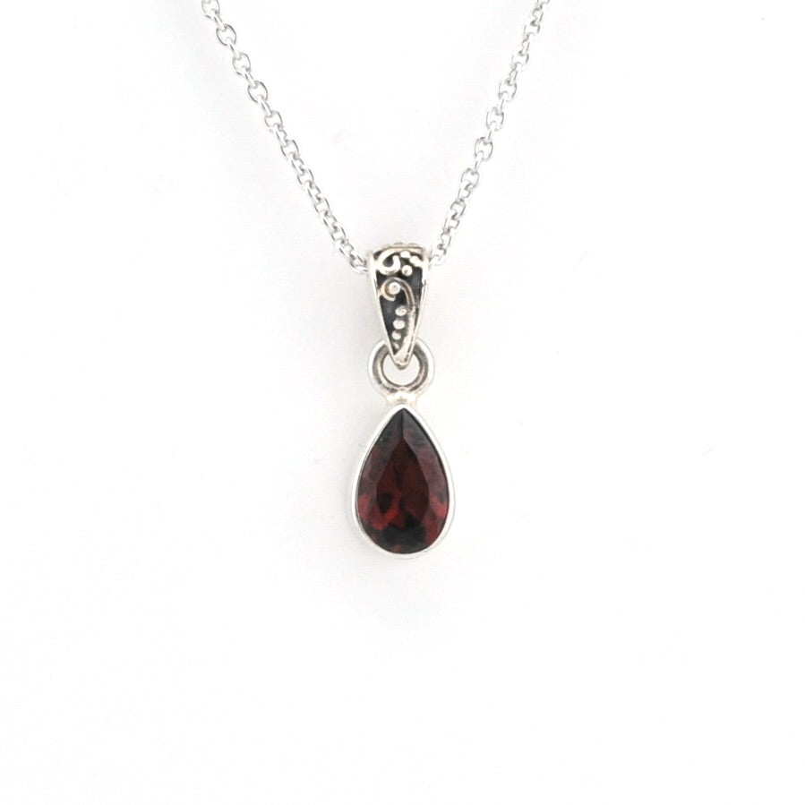 A silver teardrop pendant necklace featuring a faceted dark red gemstone, suspended from a delicate silver chain against a plain white background.
