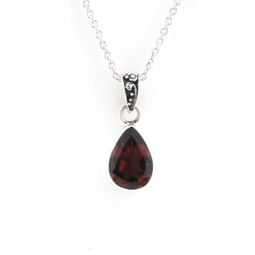 A silver teardrop pendant necklace featuring a faceted dark red gemstone, suspended from a delicate silver chain against a plain white background.