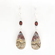 A pair of teardrop-shaped dangle earrings featuring natural agate stone inlays with earthy brown, beige, and gray banding, accented by small round dark red garnet beads on silver hooks, set against a plain white background.