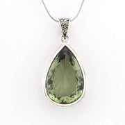 A teardrop-shaped green gemstone pendant in a silver bezel setting on a silver snake chain, shown against a plain white background.