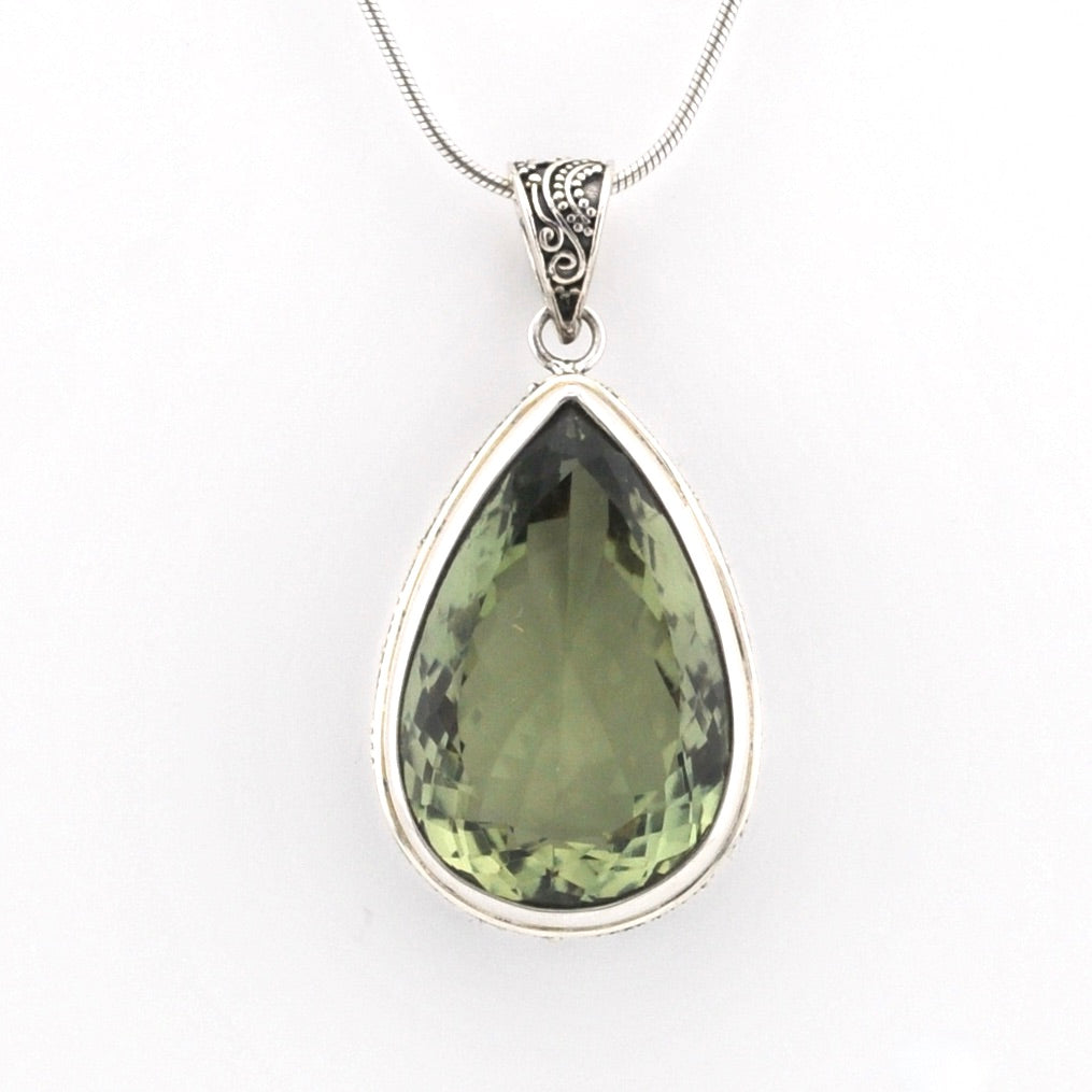 A teardrop-shaped green gemstone pendant in a silver bezel setting on a silver snake chain, shown against a plain white background.