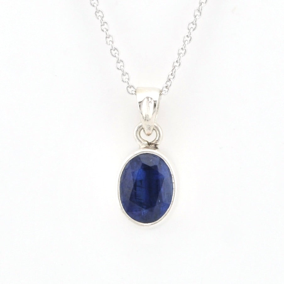 A silver pendant necklace featuring an oval-cut deep blue sapphire gemstone in a polished silver bezel setting, suspended from a delicate silver chain against a plain white background.