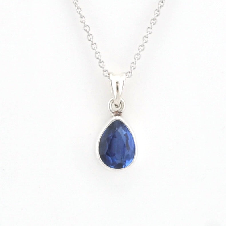 A silver pendant necklace featuring a faceted teardrop-shaped blue gemstone in a silver bezel setting, suspended from a delicate silver chain against a plain white background.