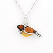 A bird-shaped pendant necklace made of silver metal and amber-colored glass, featuring a dark brown head, a translucent orange wing, and a yellow belly, suspended from a silver chain on a white background.